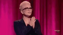 a woman wearing glasses and a suit is applauding on a stage .