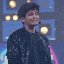 a young man in a sequined jacket is crying while standing in front of a microphone on a stage .