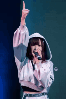 a girl in a hoodie is singing into a microphone with her hand in the air