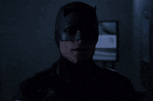 a man in a batman mask looks at the camera in the dark