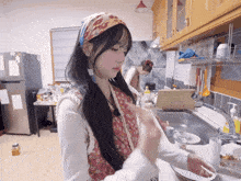 two women are washing dishes in a kitchen and one is wearing a head scarf