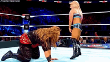 a woman is kneeling down in a wrestling ring while another woman stands in the corner .