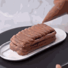 a person is frosting a cake with chocolate frosting on a white plate