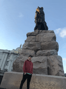 a man in a red hoodie stands in front of a statue of a man with a sword