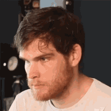 a man with a beard is wearing a white shirt and looking to the side