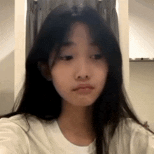 a girl with long black hair is wearing a white shirt and looking at the camera .