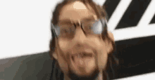 a man with dreadlocks and glasses is making a funny face with his tongue out .