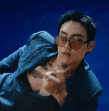 a man wearing sunglasses and a blue jacket has a tattoo on his chest