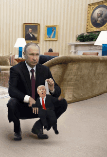 a man in a suit and tie is squatting down holding a small trump doll
