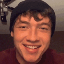 a young man wearing a black beanie and a red shirt smiles for the camera