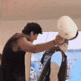 a man in a black tank top is putting a white hat on another man 's head