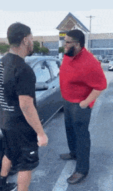 two men are standing next to each other in a parking lot and talking to each other .