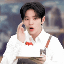 a man in a white shirt is holding a cake with strawberries on it