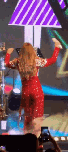 a woman in a red dress is standing on a stage with her arms in the air .