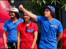 three men wearing blue shirts and red shirts are standing next to each other in front of a pink float .