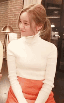 a woman wearing a white turtleneck sweater and orange skirt