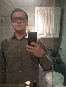 a young man wearing glasses takes a selfie in front of a bathroom mirror