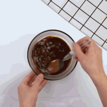 a person is mixing a brown liquid in a glass bowl with a spoon