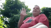 a man in a red shirt with a bird on it is waving his hand