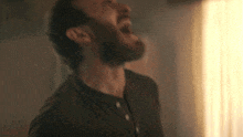 a man with a beard is screaming with his mouth wide open in a dark room .