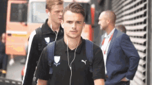 a man wearing headphones and a puma shirt walks down a street .