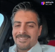 a man with a mustache is sitting in a car and smiling .
