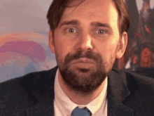 a man with a beard in a suit and tie looks at the camera