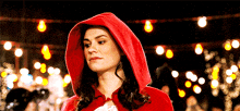 a woman in a red hooded cape is standing in front of a string of lights