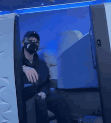 a man wearing a mask is sitting in a blue airplane seat
