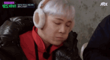 a man wearing ear warmers and a red jacket is sitting in front of a sign that says jttc