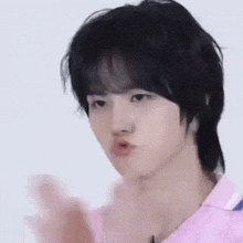 a young man with black hair is wearing a pink shirt and making a face .