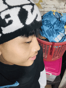 a boy wearing a black and white beanie with the letter e on it stands in front of a laundry basket