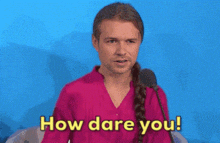 a man in a pink shirt is talking into a microphone and says how dare you