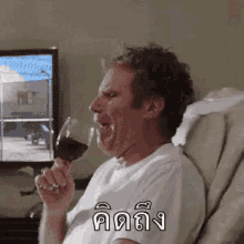 a man is drinking a glass of wine while sitting in a chair in front of a television .