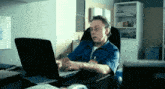 a man in a blue shirt is typing on a laptop computer