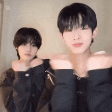 two young men are standing next to each other and one of them is wearing a black jacket .