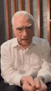 an older man in a white shirt is sitting on a couch and talking .