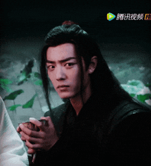 a man with long hair is holding something in his hand with chinese writing on the bottom right corner