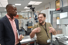 a man talking to another man in front of a machine that says danger on it