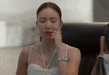a woman in a white dress is sitting in a chair with her eyes closed and her hand on her chin .