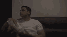 a man in a white shirt is sitting on a black couch holding a bag of chips