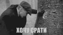 a black and white photo of a man looking at a tree trunk with the words " хочу спати " written on the bottom