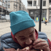 a man wearing a blue beanie is eating a sandwich outside