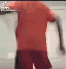 a man in a red shirt and shorts is dancing on a tik tok video .