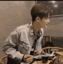 a man in a denim jacket is sitting at a table eating food