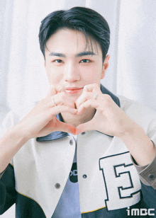 a young man wearing a jacket with the letter e on it is making a heart shape with his hands