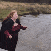 a woman in a red dress and black cape is standing in a river