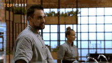 a man in a top chef uniform is standing in front of a window