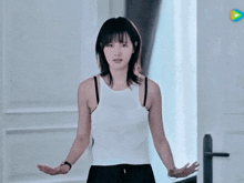 a woman in a white tank top is standing in front of a door with her arms outstretched .