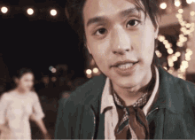 a young man wearing a green jacket and a brown tie looks at the camera